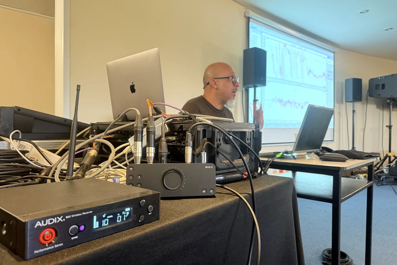 Mesa de medición del curso de Smaart 2026: receptor inalámbrico, interfaz y el instructor frente a la proyección del software