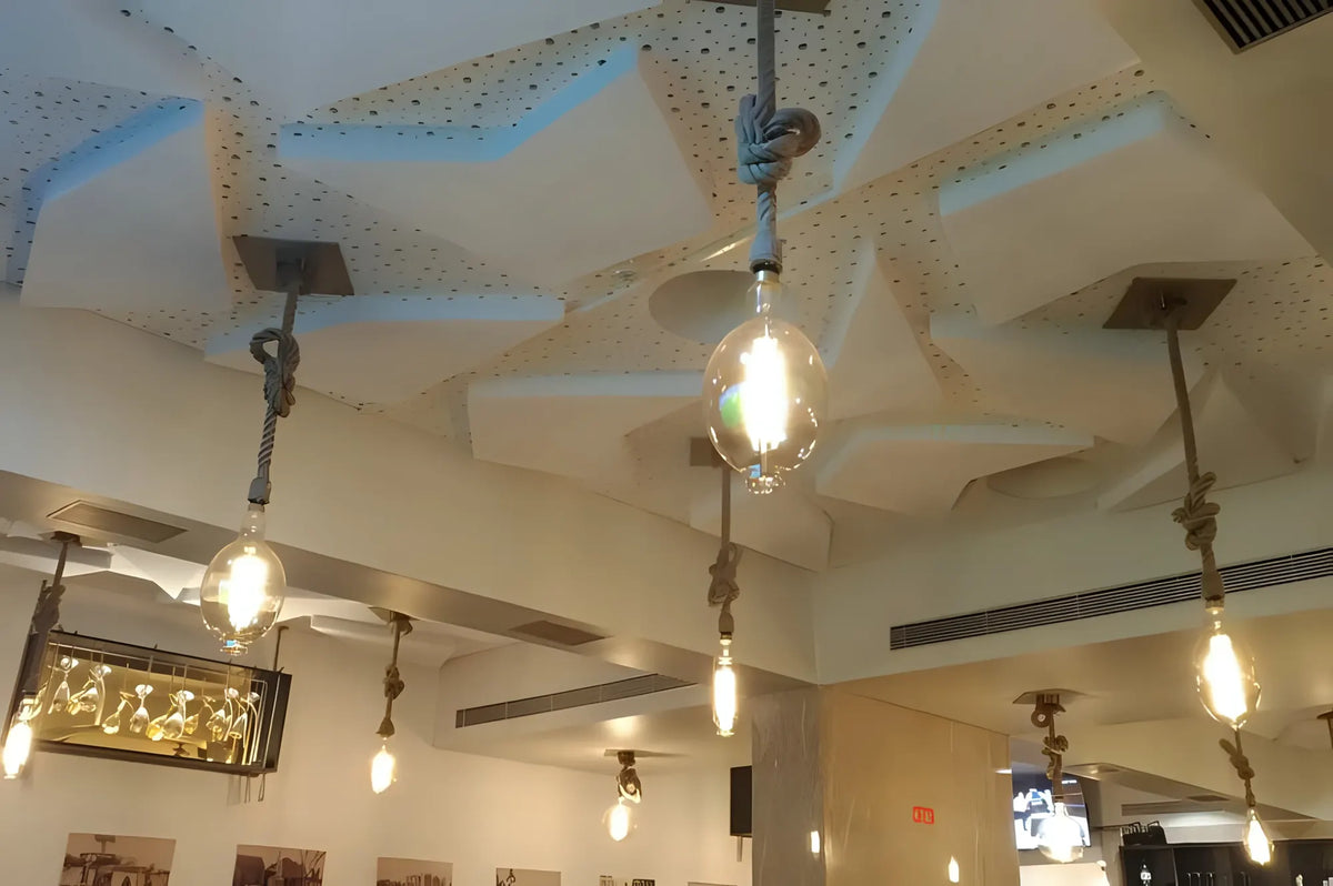 Techo de restaurante con paneles acústicos triangulares ISINAC suspendidos entre lámparas colgantes