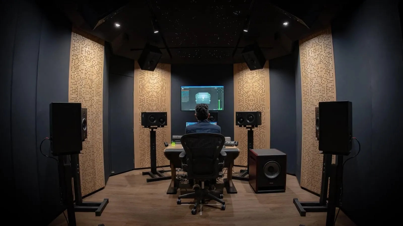 Sala de mezcla inmersiva con monitores en pedestales, subwoofer y paneles acústicos de madera perforada